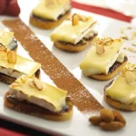 Elegant pastry desserts on white plate with yellow glaze, sliced almonds, and cocoa powder, arranged on red-trimmed surface.