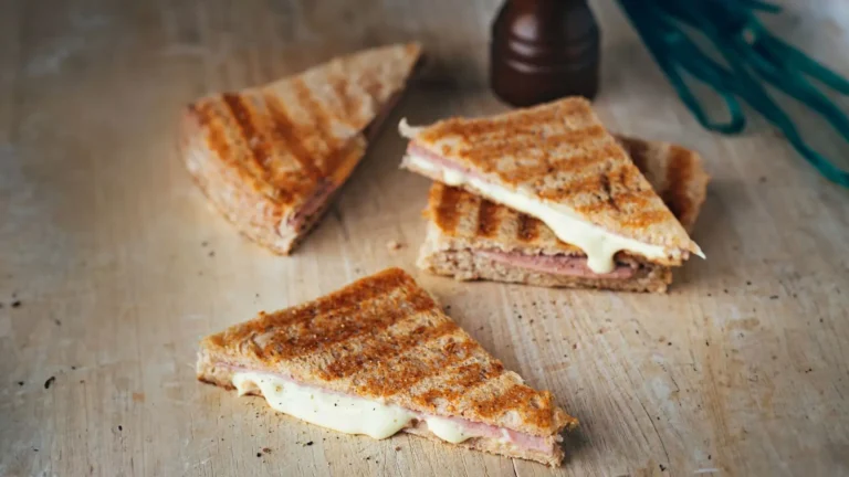 Three triangular sandwiches with cinnamon-sugar coating and melted cheese filling on a wooden surface with a dark bottle nearby.