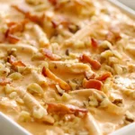 Creamy peanut butter dip in a white bowl topped with chopped peanuts and bacon bits.