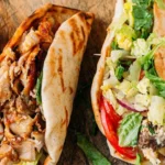 Three stuffed pita sandwiches on parchment paper with white tzatziki sauce and tan dressing in small bowls nearby.
