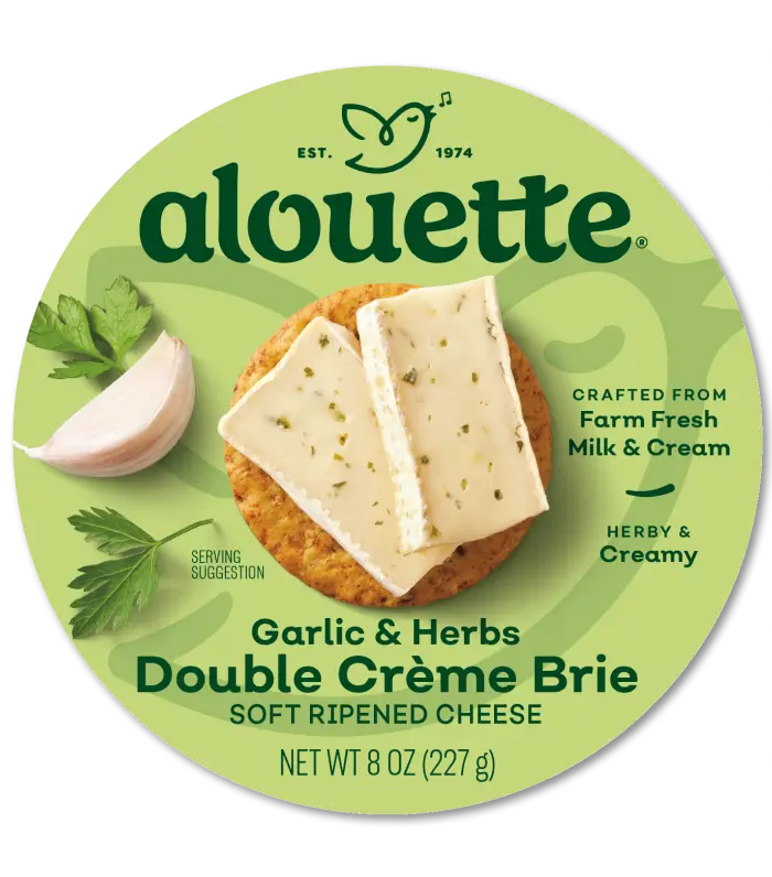 Alouette Garlic & Herbs Double Creme Brie cheese package, 8 oz, with soft ripened cheese slices and fresh herbs on green circular label.