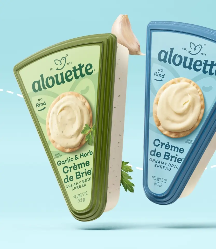 Two Alouette Crème de Brie spread packages on light blue background: green box with Garlic & Herb flavor and blue box with plain flavor, each displaying a cracker with creamy spread.
