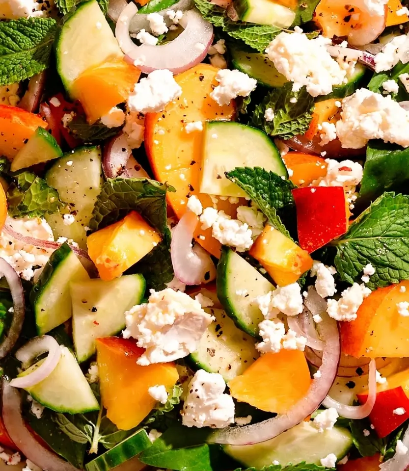Colorful salad with cucumbers, bell peppers, red onions, crumbled feta cheese, fresh mint, and black pepper seasoning.