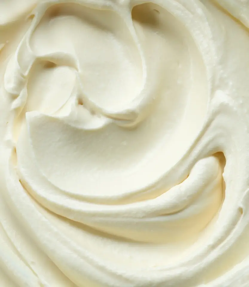 Close-up of creamy white whipped cream or frosting with smooth, swirled peaks and ridges.