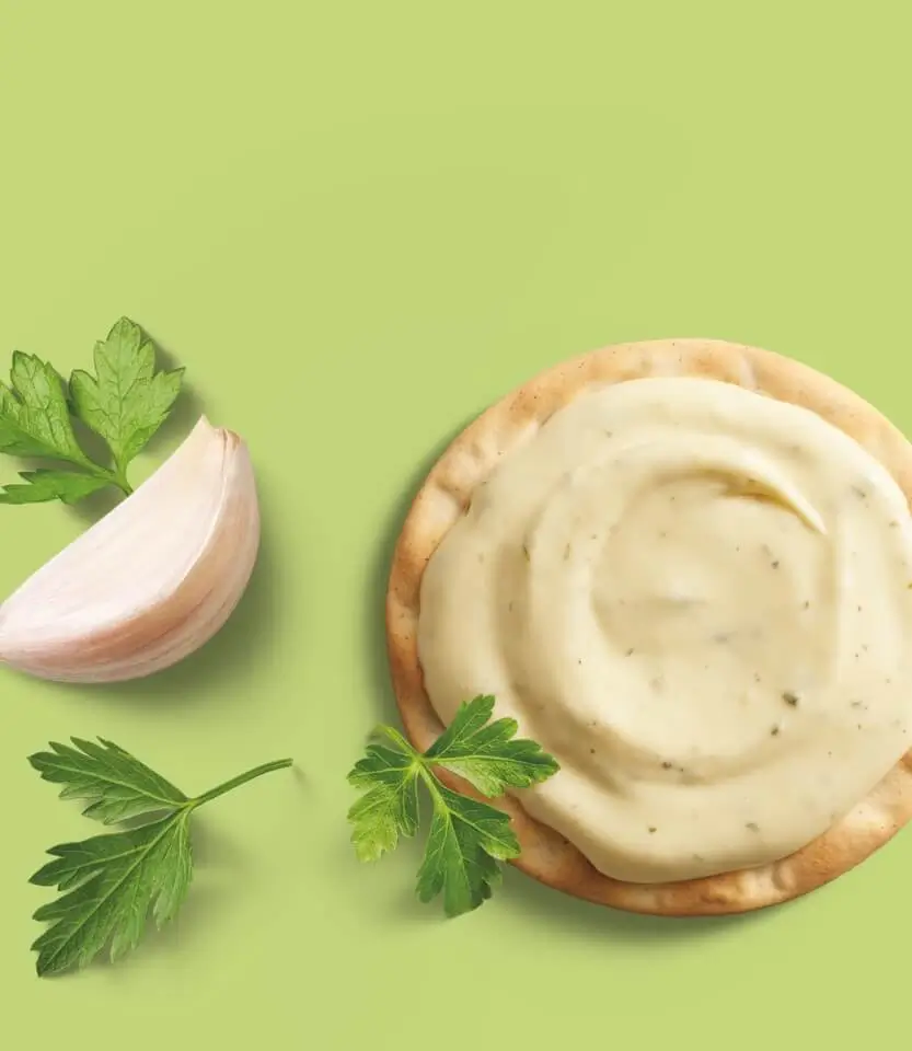 Creamy herb dip in a bowl with fresh parsley leaves and a sliced onion on a lime green background.