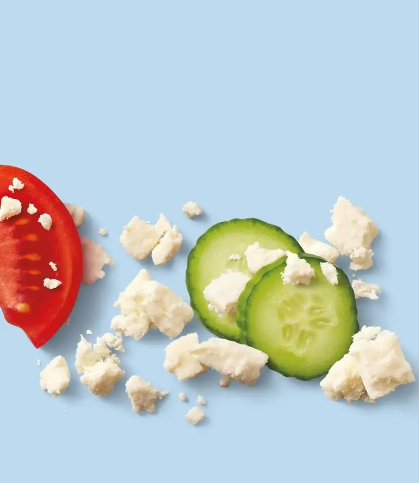 Fresh tomato slice, cucumber slices, and crumbled feta cheese on a light blue background.