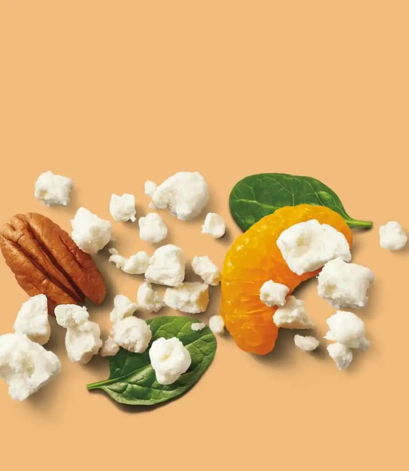 Popcorn, pecan nut, orange citrus slice, and green leaves arranged on a beige background.