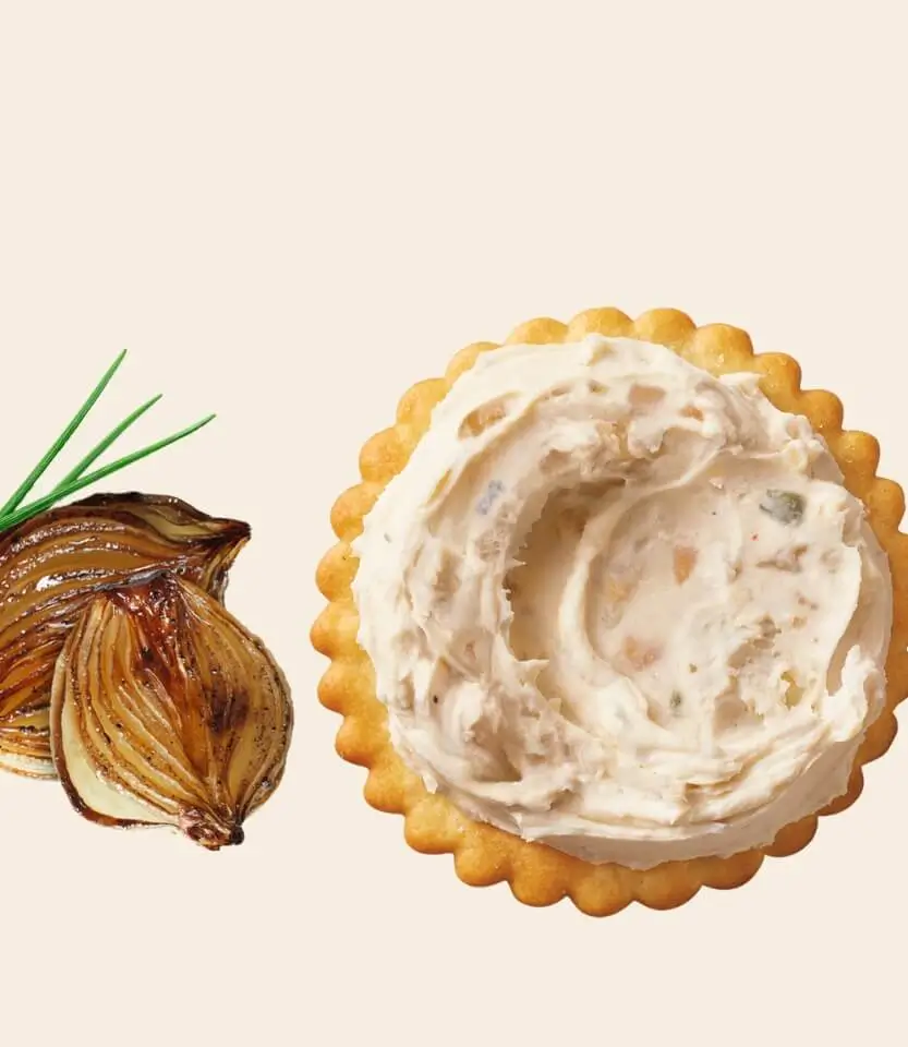 A sliced red onion with green sprouts next to a round cracker topped with creamy dip containing onion pieces.