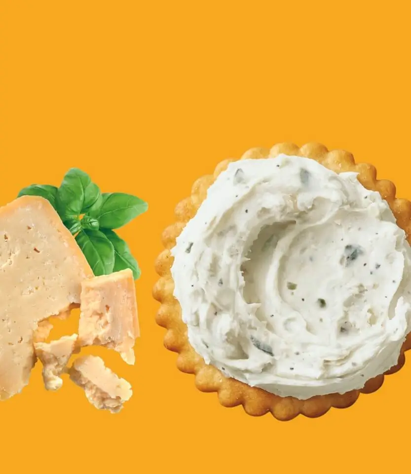 Two scalloped-edge cookies on yellow background: one with peachy frosting and basil leaf, one with white herb-flecked frosting.